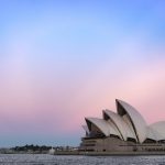 The distinctive white sails of Sydney Opera House in the bottom right, with a pink and blue sky behind